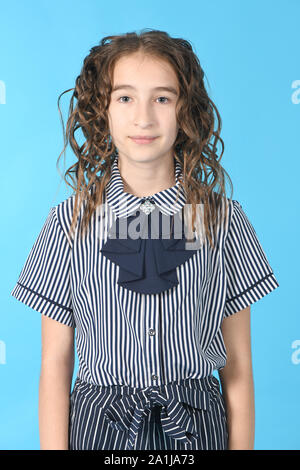 Portrait of adorable smiling schoolgirl with curl hair, standing isolated on a blue background. High resolution photo. Full depth of field. Stock Photo