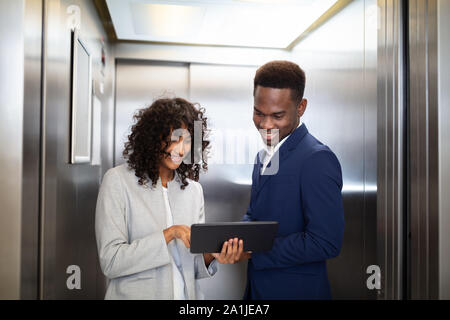 Businesspeople Discussing Standing Inside Elevator At Work Stock Photo