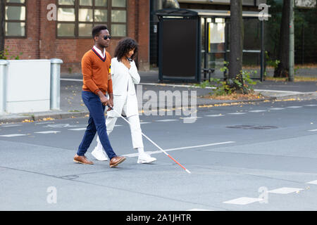 Young Woman Assisting Blind Man On Street Stock Photo