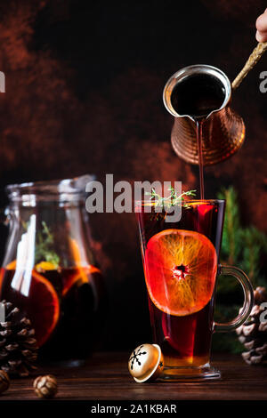 Mulled wine a warm drink made of red wine, citruses and spices in a glass on a wooden table with decorations. Mulled wine pouring into a glass Stock Photo