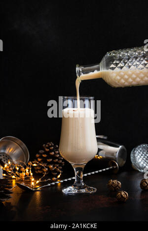 Eggnog traditional Christmas alcoholic drink with cinnamon and nutmeg. Eggnog pouring from a bottle into a glass. Winter holidays mood Stock Photo