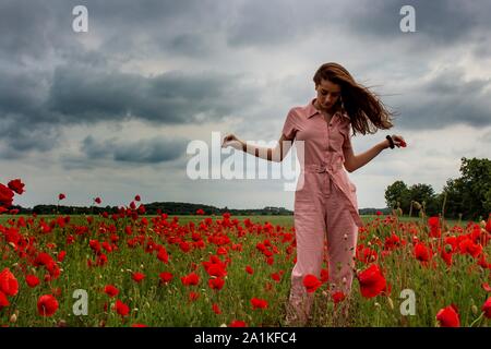Girl in pink with long hair  stood in a red Poppy field Stock Photo