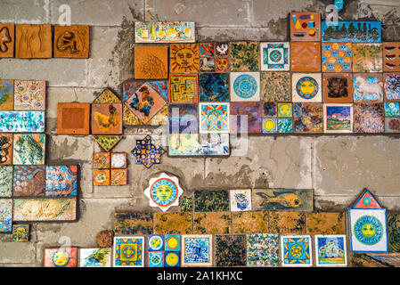 Riomaggiore, Cinque Terre, Italy - August 17, 2019: Decoration of miniature embossed tiles with color patterns for folk motifs. Image of fish, gulls, Stock Photo
