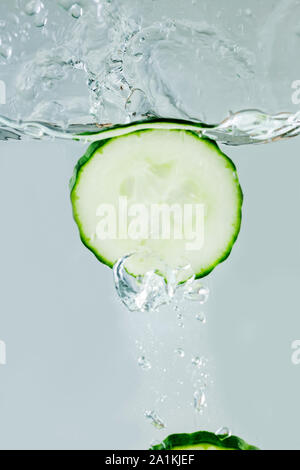 Side view of a dipping cucumber slice in water with waves and rising air bubbles. Stock Photo