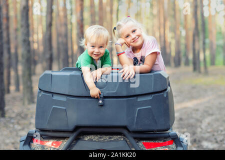 Cute adorable caucasian blond siblings having fun during atv 4x4 off-road adventure trip amog coniferous pine forest on brigh sunny day. Little boy Stock Photo