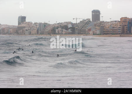 Local kids on surf boards waiting for the perfect wave to surf in the middle of the city of Las Palmas de Gran Canaria Stock Photo