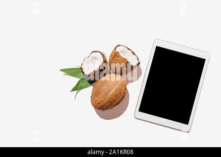Tablet device with blank screen next to coconuts and green leaves on white background, flat lay composition. Stock Photo