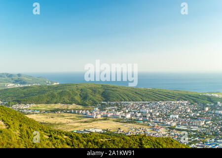 Scenic view of Black sea coastline, green forest areas, grass fields in the lowland and cityscape of Gelendzhik resort in Russia. Residential houses. Stock Photo