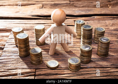 Stacked Golden Coins Around By Wooden Human Figure Over Desk Stock Photo