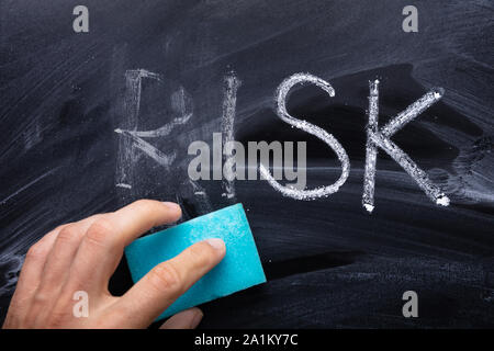 Close-up Of Person's Hand Erasing Risk Text With Blue Sponge Stock Photo
