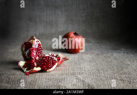 Half pomegranate and raw pomegranates on a brown sackcloth background. Rustic style. Stock Photo