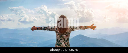 Girl traveling in mountains alone, standing with hands up achieving the top, welcomes a sun. Walking outdoors, woman hiker on mountain top. Wanderlust Stock Photo