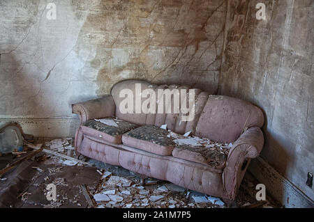 An old pink sofa sits abandoned in the rubble of a ruined house. Stock Photo