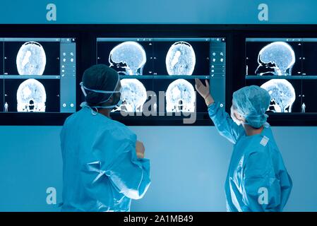 Surgeons looking at magnetic resonance imaging (MRI) brain scans during brain surgery. Stock Photo