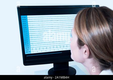 Female medical professional looking at EEG (electroencephalogram) results on a screen. Stock Photo