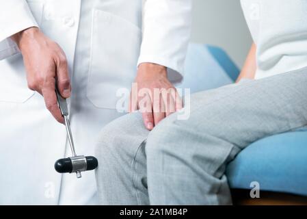 Female doctor testing patient's reactions by tapping her knee with a reflex hammer. Stock Photo