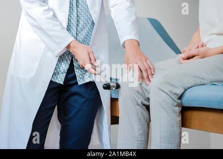 Female doctor testing a patient's reactions by tapping her knee with a reflex hammer. Stock Photo