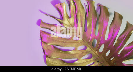 Monstera leaf painted in gold paint with trendy duotone neon color on pastel pink. Abstract pattern for design and space for text. Stock Photo