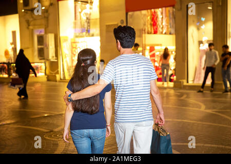 The boy grabs the girl's shoulder and walks around the city in the evening . They go shopping in the city. rear view Stock Photo