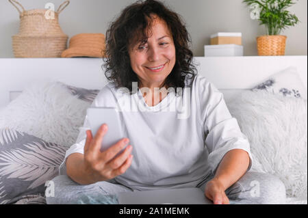 A woman with a laptop is sitting on the bed. Modern business lady at home. Photo in light colors Stock Photo