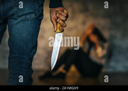 Concept on the topic of domestic violence. A man with a knife in the room threatens the girl Stock Photo