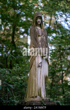 Stone statue of a mourning woman as decoration on a shady graveyard in the woods Stock Photo