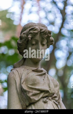 Stone statue of a mourning woman as decoration on a shady graveyard in the woods Stock Photo
