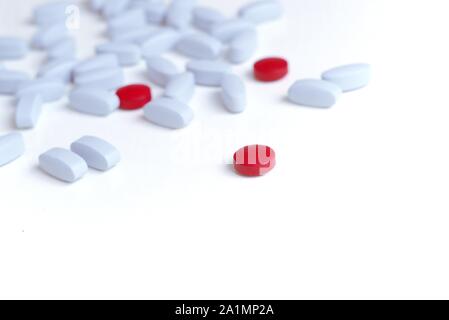 Single red pill shown prominently among light blue pills on white background. Stock Photo