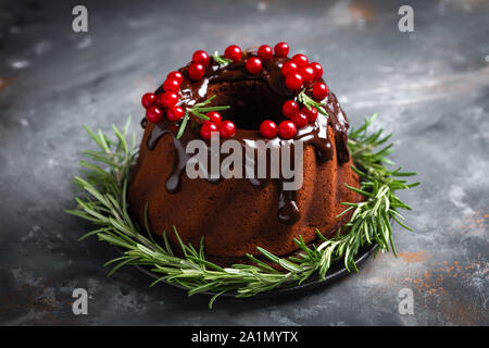 Christmas chocolate bundt cake with glaze decorated with fresh berries and rosemary. Winter baking at Xmas or New Year with decorations on dark backgr Stock Photo