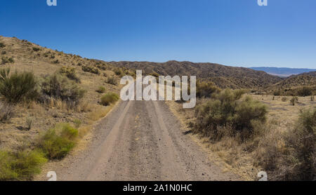 Gravel road leads through the brush and grass of Carrizo Plain National Monument. Stock Photo