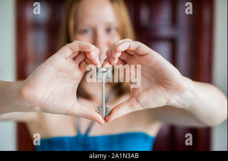 Women's hands hold house key in the form of heart on the background a wooden door. Owning real estate concept Stock Photo