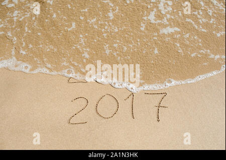 New Year 2017 is coming concept - inscription 2016 and 2017 on a beach sand, the wave is almost covering the digits 2016 Stock Photo
