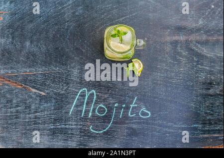 glass of mojito with lime and mint ice cube close-up on dark wood background. The inscription in chalk MOJITO Stock Photo