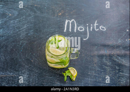 glass of mojito with lime and mint ice cube close-up on dark wood background. The inscription in chalk MOJITO Stock Photo