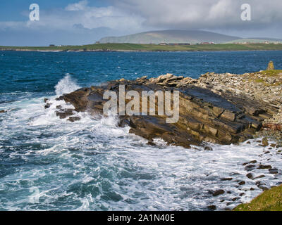 Wave action on inclined sandstone rocks on the south Shetland coast near Sumburgh Head, showing rock debris swept by waves on the right. The hill of F Stock Photo