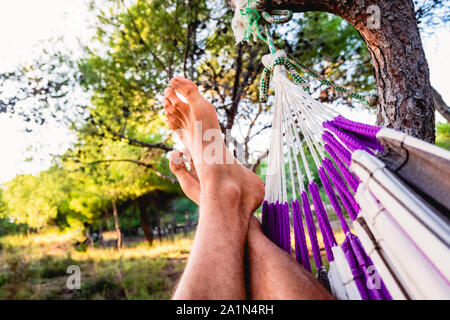 A man takes a nap lying in a hammock, from below only his feet. Stock Photo