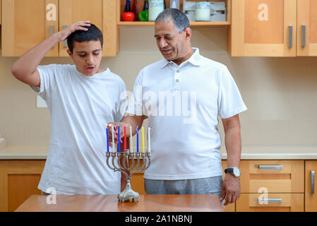 Happy family is lighting a candle celebrating together Jewish holiday Hanukkah. Jewish Dad and teenager son or grandfather with grandson lighting Chanukkah Candles in a menorah for the holdiay Stock Photo