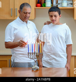 Happy family is lighting a candle celebrating together Jewish holiday Hanukkah. Jewish Dad and teenager son or grandfather with grandson lighting Chanukkah Candles in a menorah for the holdiay Stock Photo