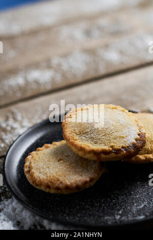 Three mince pies on a black plate on a rustic wooden table with snow Stock Photo