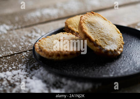 Three mince pies on a black plate on a rustic wooden table with snow Stock Photo