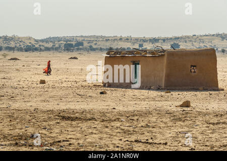 Jaisalmer, India - February 14, 2019: Indian woman in red sari grazing cows near traditional village at Thar desert