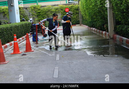 Bangkok, Thailand - September 28, 2019: Two female workers are cleaning the floor, one uses high pressure cleaner spraying water while the other uses Stock Photo