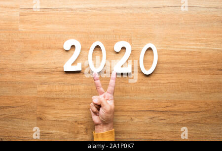 2020 new year celebration concepts with text number and human hand showing V sign on wood background. inspiration and motivation ideas Stock Photo