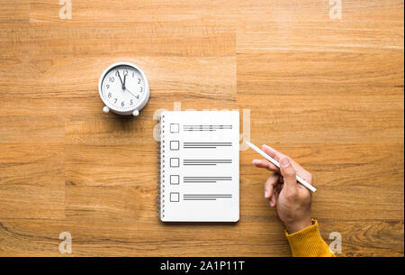 Exam and time management concepts with male hand holding pencil and paper sheet on wood table. Stock Photo