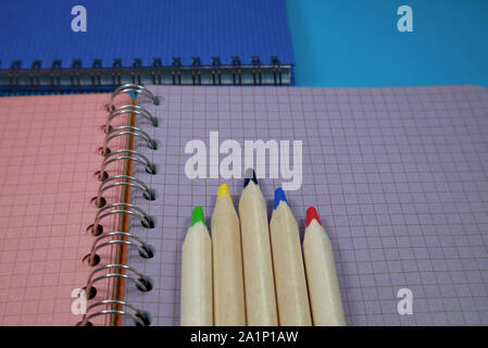 Pencils crayons lying on wire bound open notebook ruled with squares with green and purple pages in a conceptual image for business or education Stock Photo