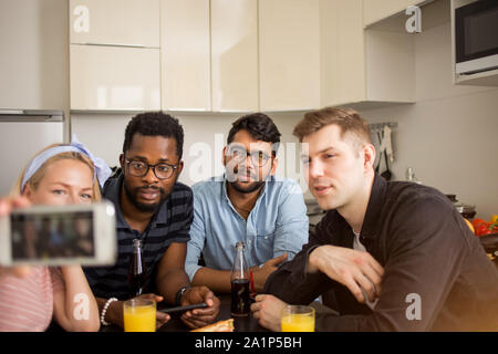 Multiracial group of friends taking selfie while sitting at table and having lunch. Friendship, leisure and technology concept. Cheerful students havi Stock Photo