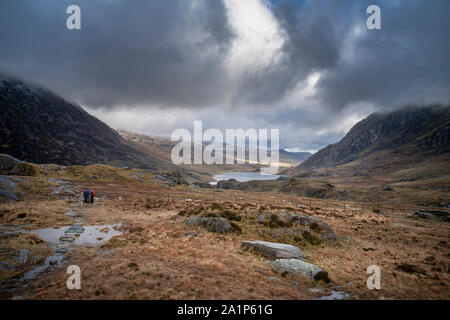 Hikers in Ogwen Valley Winter landscape with snowcapped Pen Yr Ole Wen and Tryfan mountains with dramatic light Stock Photo
