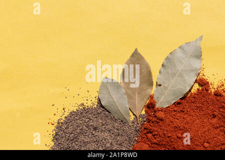 Bay leaf and two heaps of ground pepper black and red on a solid yellow background Stock Photo