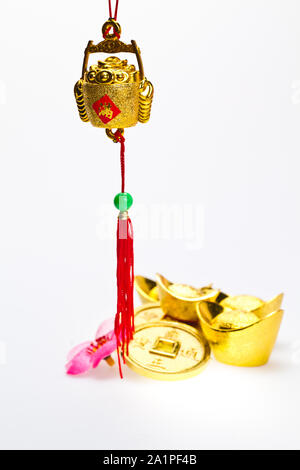 Hanging wealth pot pendant for Chinese New Year celebration with gold ingots and coins in background against white surface Stock Photo