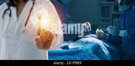 female doctor with stethoscope hand pointing touching virtual screen interface button with group of surgeon work in operation room at hospital Stock Photo